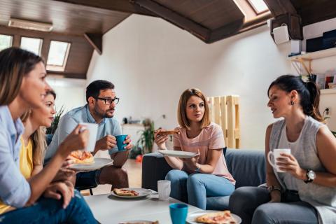 mensen die koffie drinken en taart eten in de zetel. Ze zijn in gesprek met elkaar. 