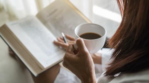 Vrouw die een boek aan het lezen is met een koffie in haar hand